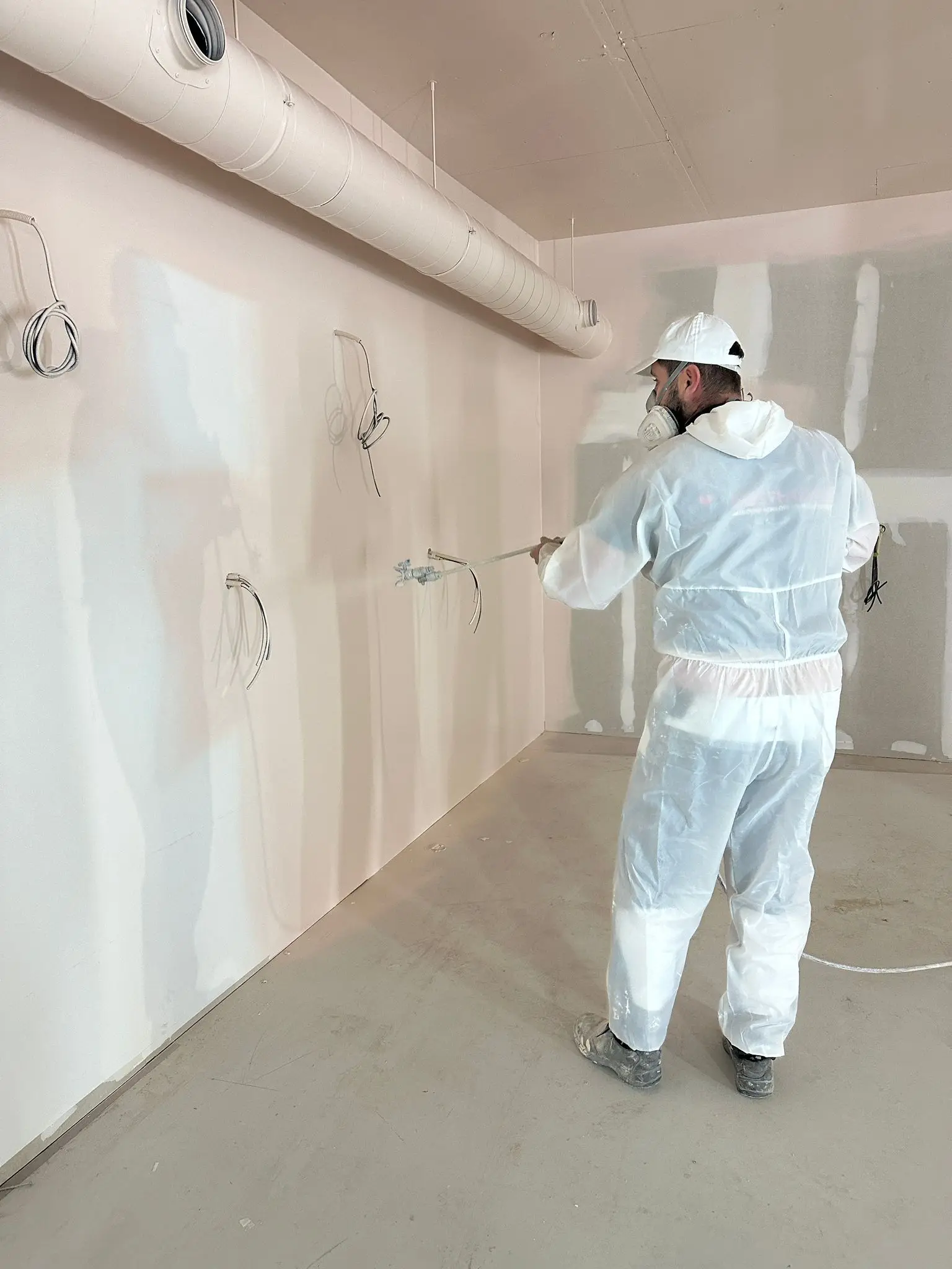 Schilder spuit met een airless installatie een wand in een leeg nieuwbouwpand