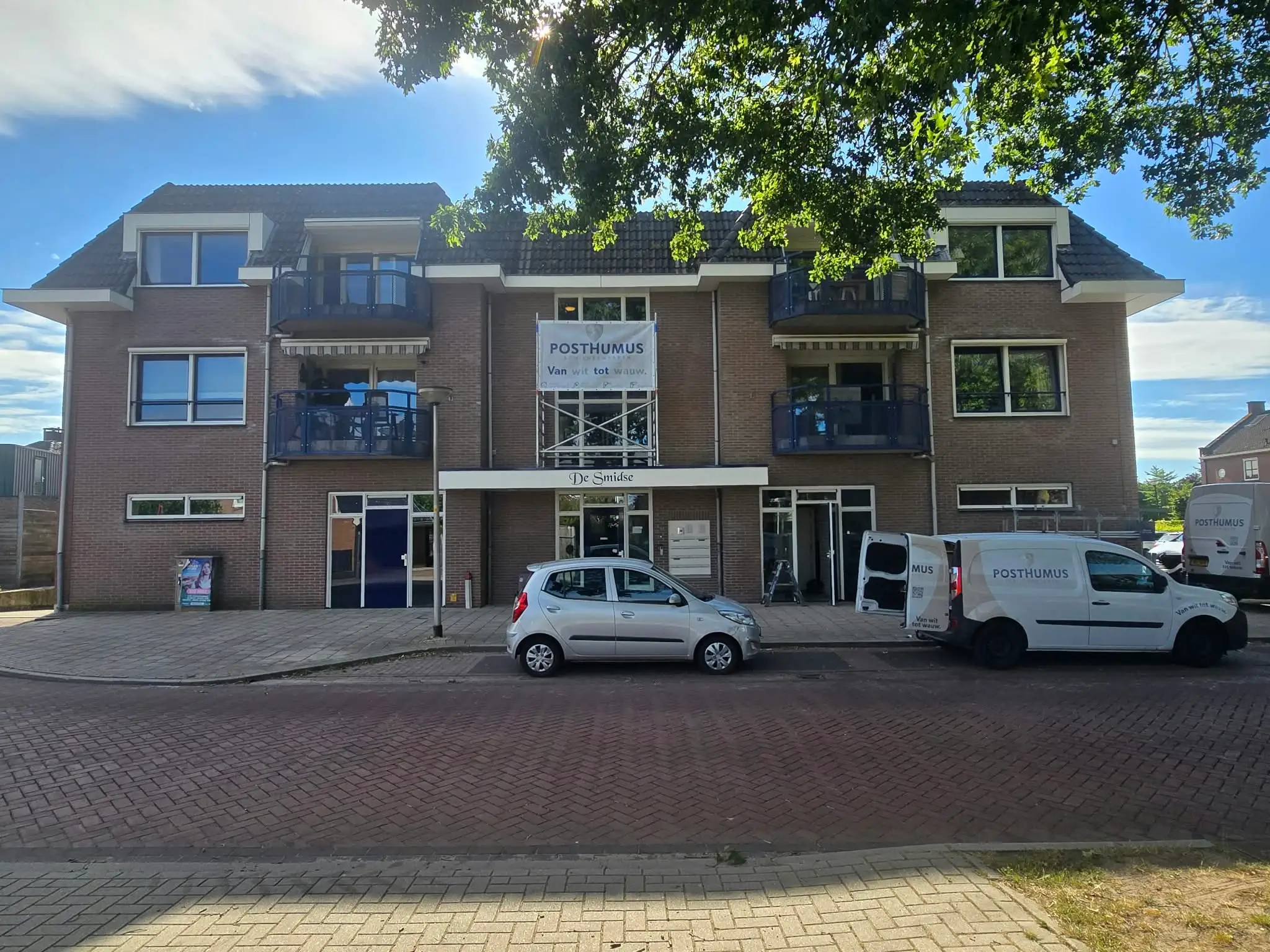 Appartementencomplex met twee bedrijfsbussen van Posthumus Schilderwerken ervoor