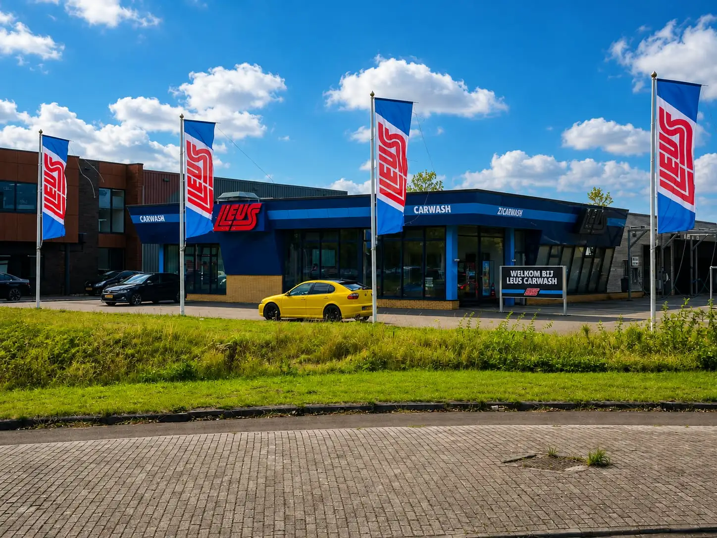 Bedrijfspand van een carwash met blauwe gevelbeplating en vlaggenmasten, na buitenschilderwerk