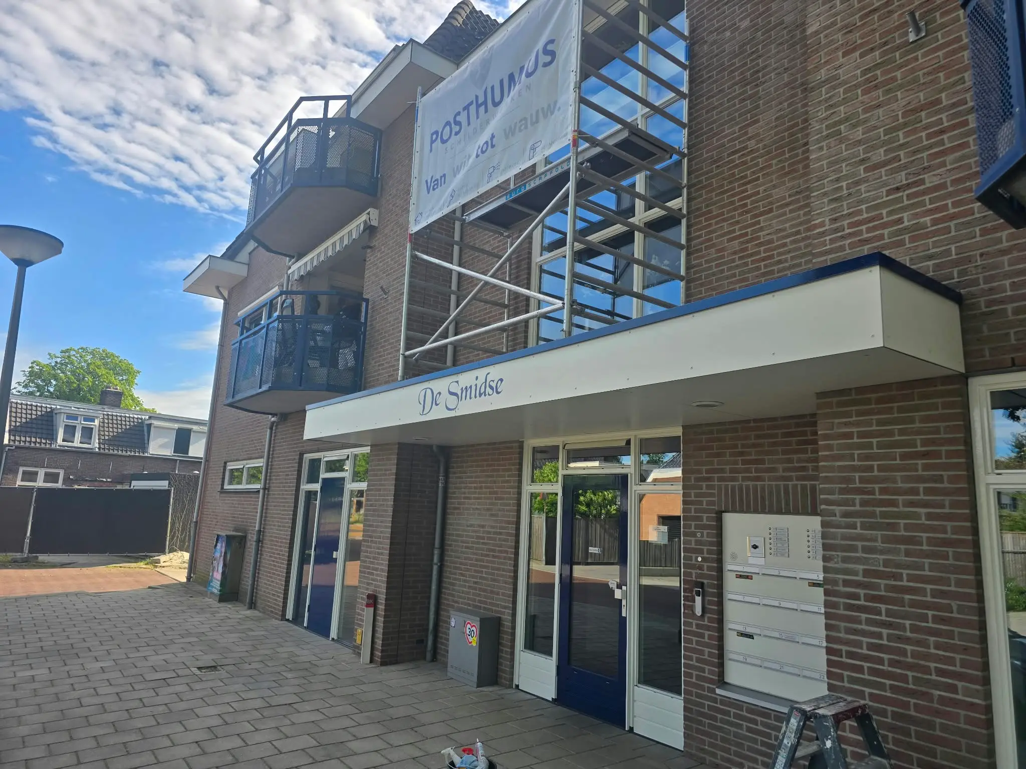Bedrijfsverzamelpand met steiger langs de gevel en een doek van de schilder eraan