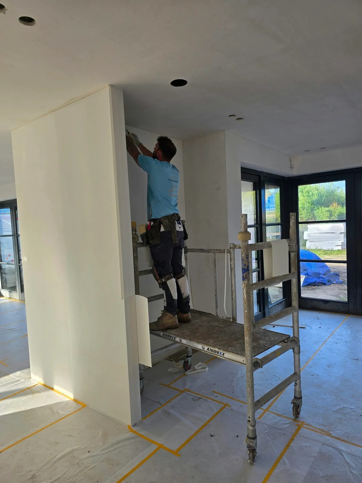 Schilder van Posthumus Schilderwerken werkt vanaf een rolsteiger aan een binnenwand in een woning