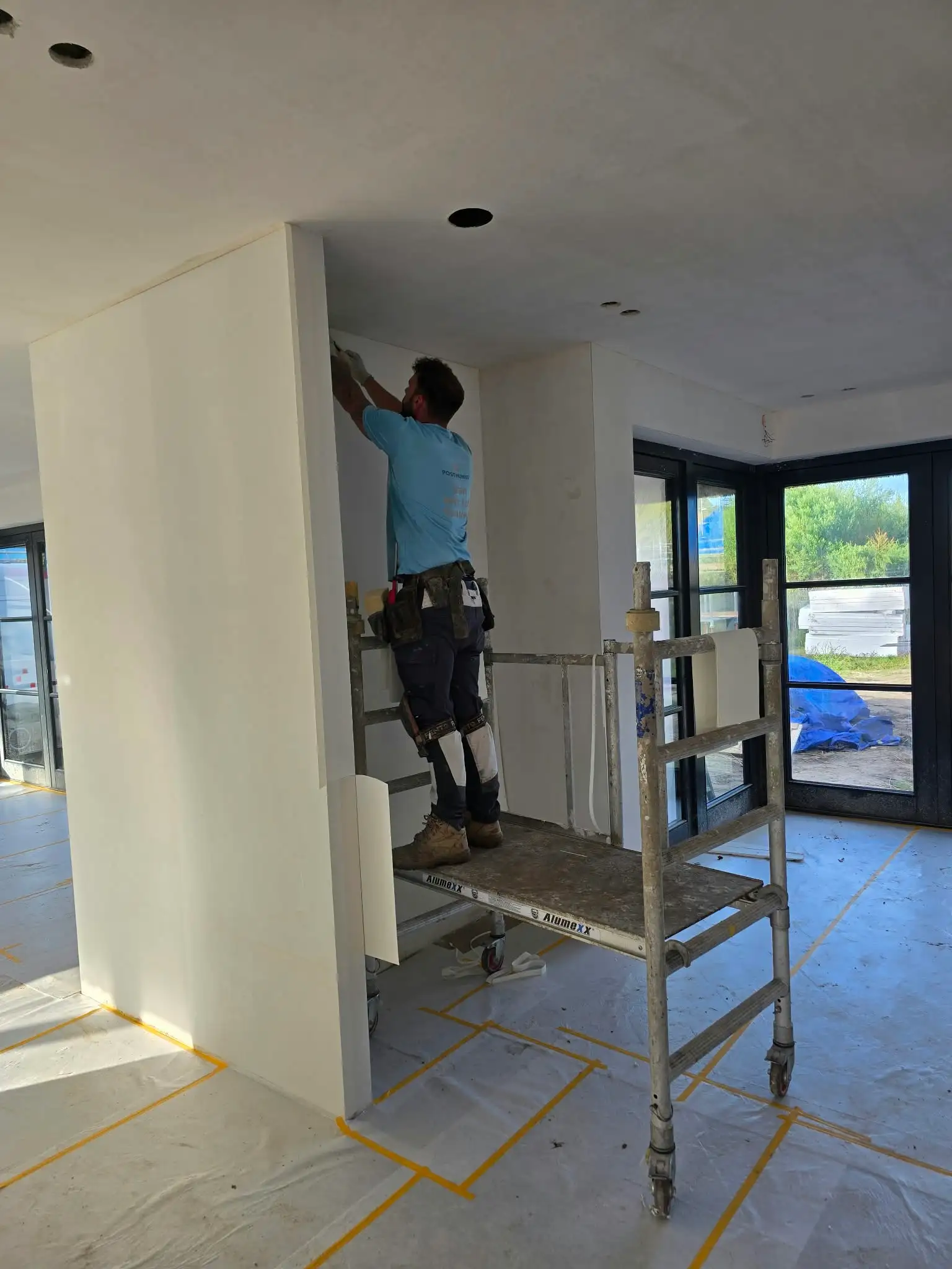 Schilder van Posthumus Schilderwerken werkt vanaf een rolsteiger aan een binnenwand in een woning