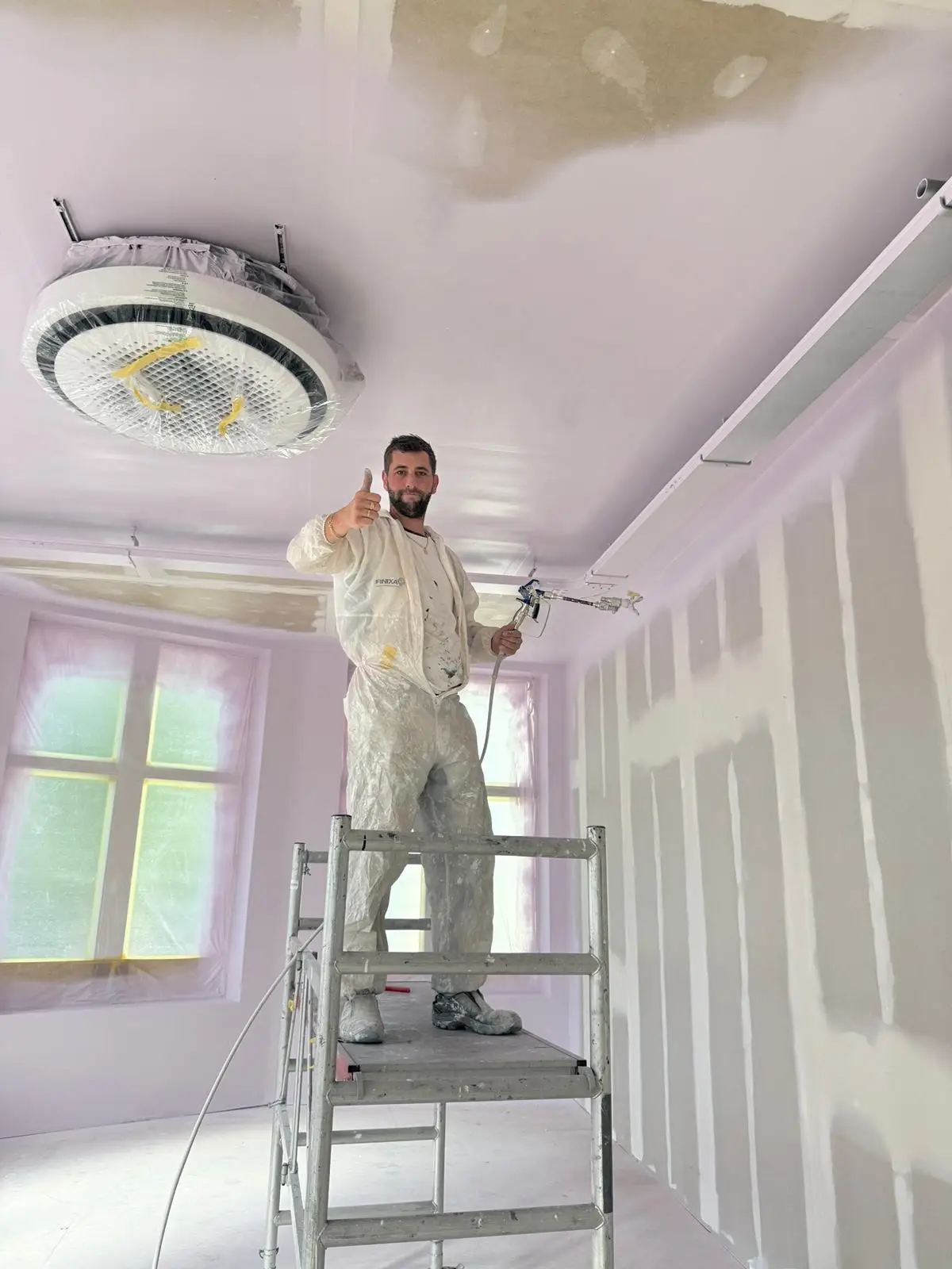 Schilder van Posthumus Schilderwerken spuit vanaf een rolsteiger een plafond in een woning