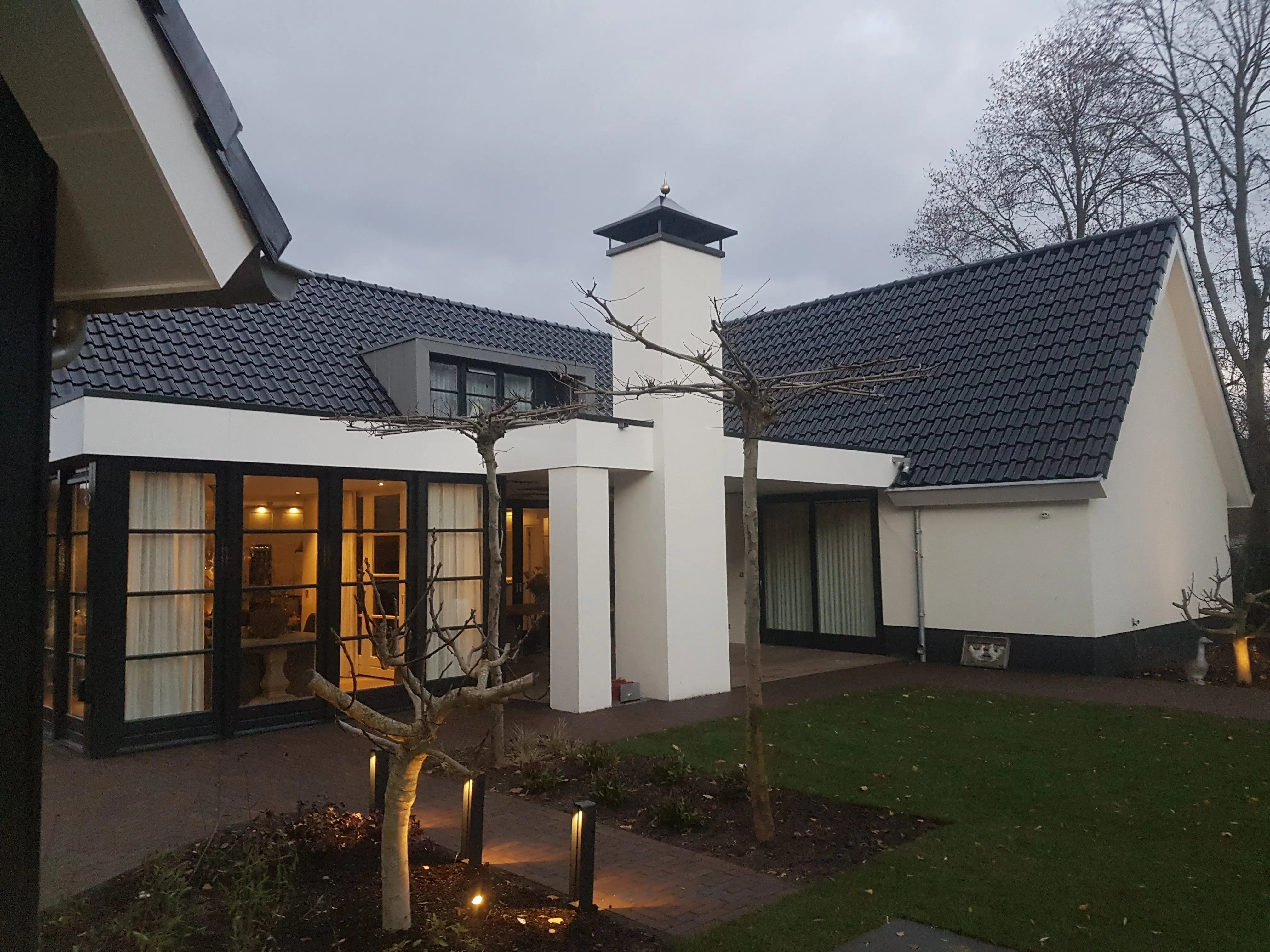 Wit gestuukte villa in de schemering met antracietgrijze kozijnen en dakgoten