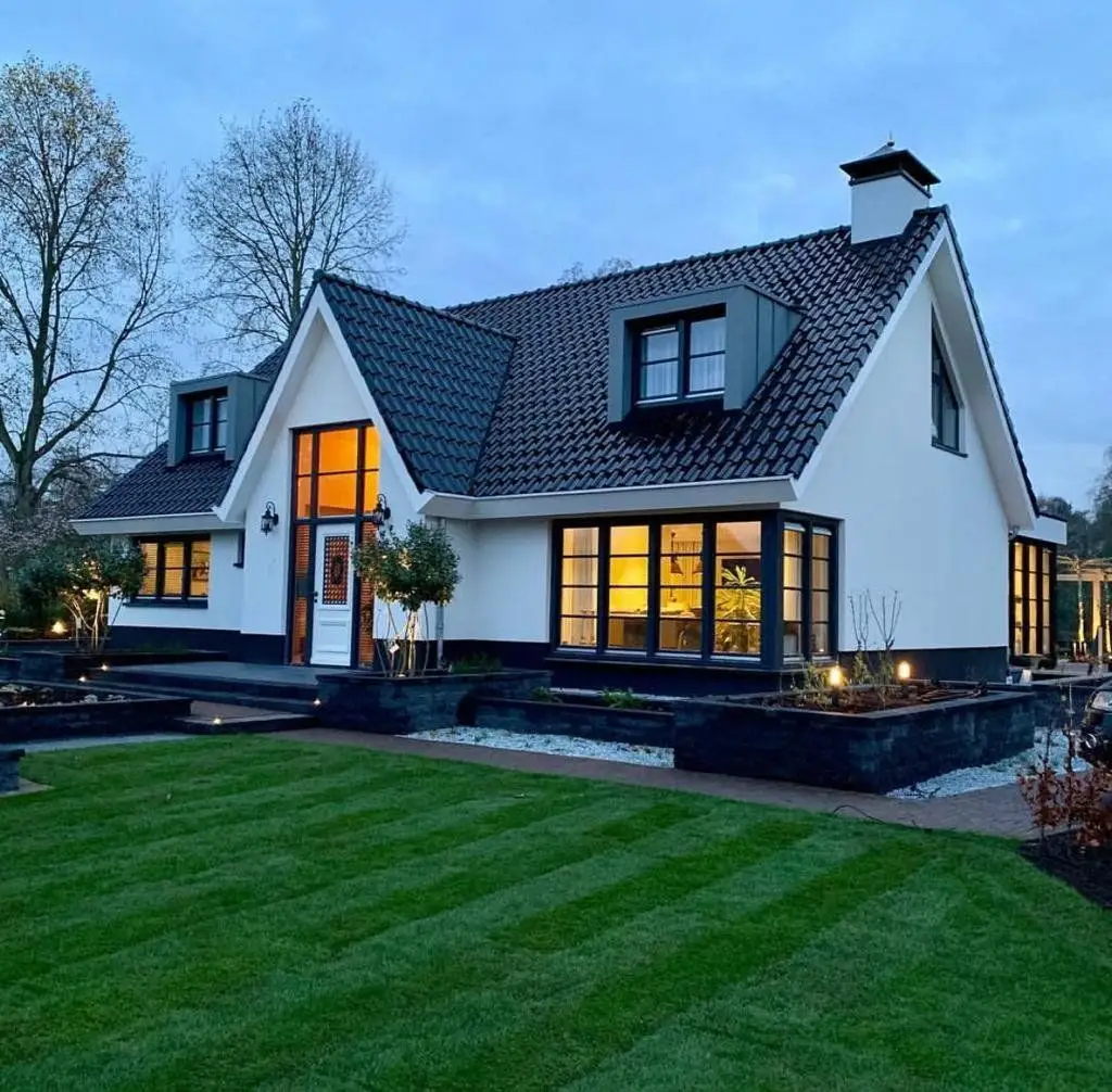 Woonhuis in de avond met verlichte ramen, houten kozijnen en luiken
